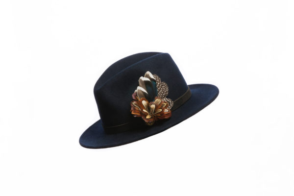 Mixed Feather Combo Hat Pin / Brooch / Lapel Pin set in a 12 bore cartridge base on a navy fedora with a brown hat band on a white background.