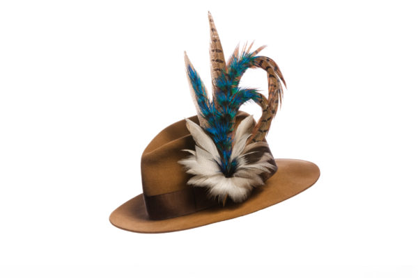 Large Peacock Blue Feather Hat Pin set in a silver cone base pinned to a tan fedora with a brown hat band on a white background.